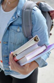 woman wearing blue denim jacket holding book